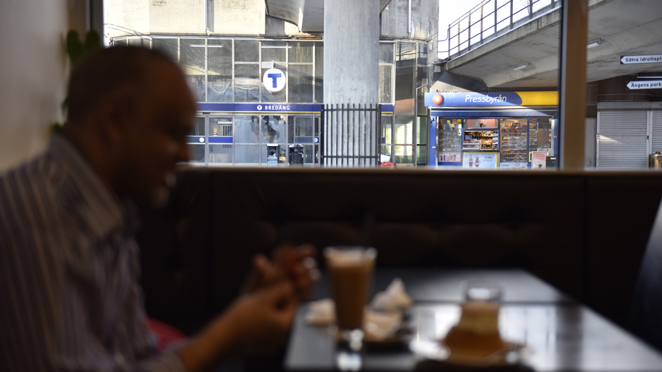 En man med ett glas kaffe framför sig. Utanför fönstret en tunnelbanestation.